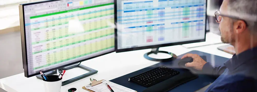 Informationssicherheitsbeauftragter arbeitet konzentriert am Computer mit zwei Bildschirmen