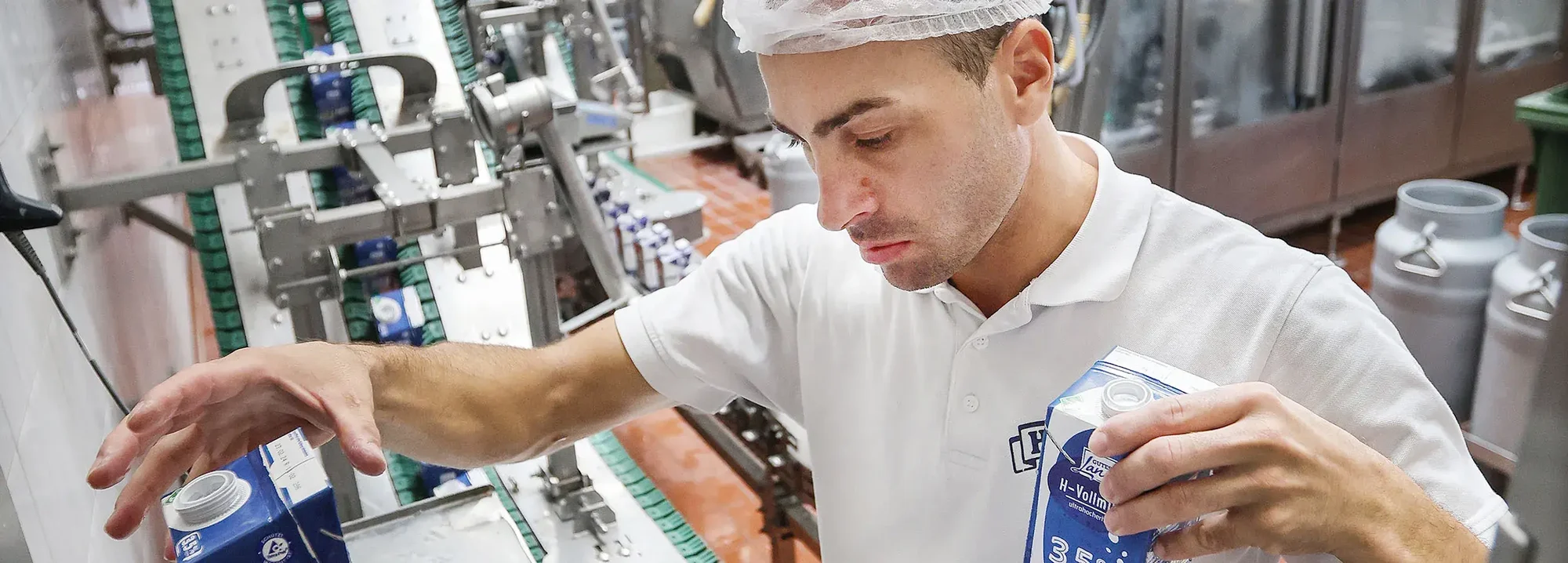 Ein Mitarbeiter der Hohenloher Molkerei steht in der Produktion und wiegt verschiedene Tetra-Paks mit Milch
