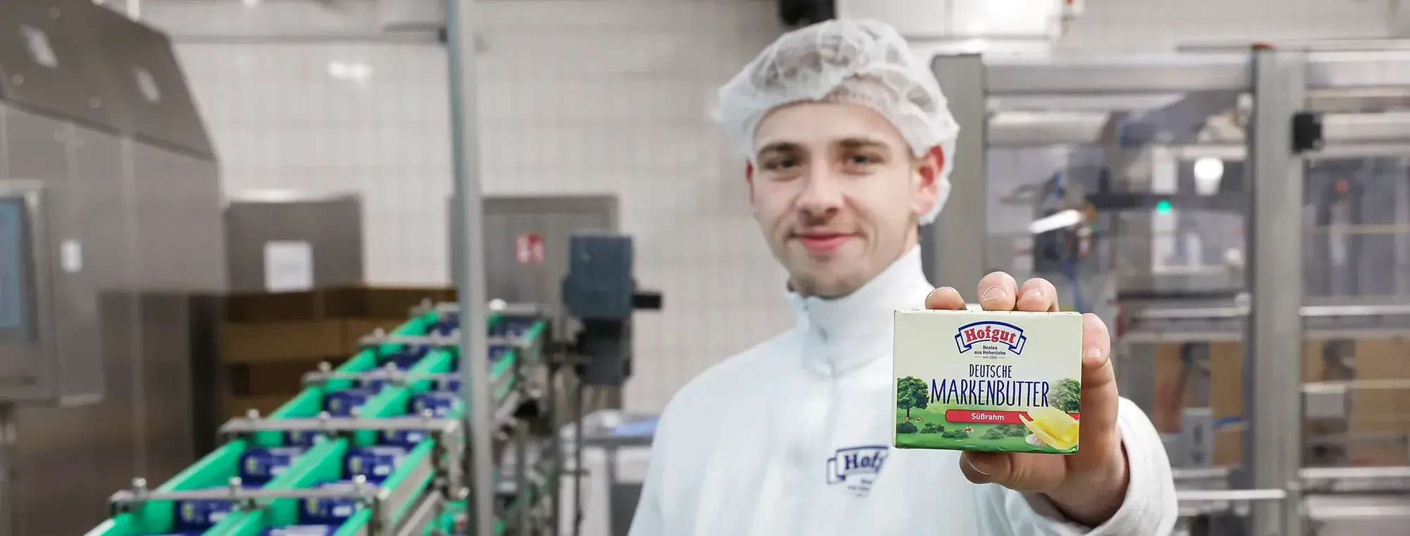 Ein Mitarbeiter der Hohenloher Molkerei in der Butterei hält einen Pack der mit DLG-Gold zertifizierten Deutschen Markenbutter süßrahm der Hohenloher Molkerei in die Kamera.