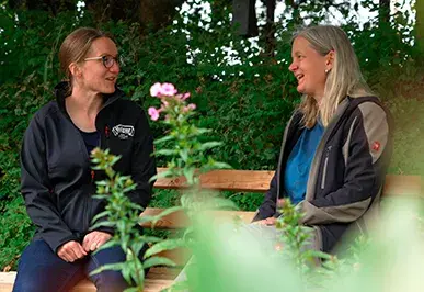Sara Hackspacker, Leiterin der Abteilung Landwirtschaft bei der Hohenloher Molkerei im Gespräch mit Landwirtin Frau Riha auf einer Bank im Grünen