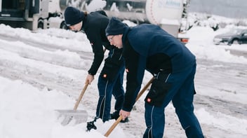 Zwei Mitarbeiter der Hohenloher Molkerei schippen Schnee auf dem Werksgelände
