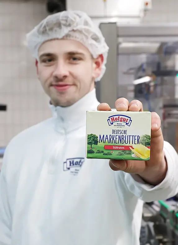 Ein Mitarbeiter der Hohenloher Molkerei in der Butterei hält stolz eine Packung Butter in die Kamera