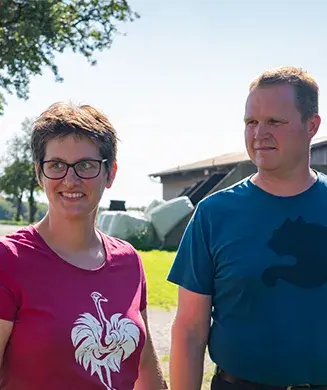 Herr und Frau Lutz stehen auf ihrem Bauernhof vor einer Wiese mit einer Scheune