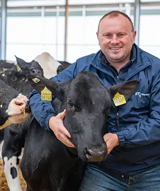 Der Landwirt Herr Nürnberger steht im Stall bei seinen Kühe und umarmt lächelnd die Kuh direkt neben ihm