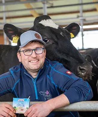Manuel Gärtner, Mitgesellschafter des Hof Nürnbergers, lehnt an einem Gatter im Stall, während ihm eine Kuh über die Schulter schaut