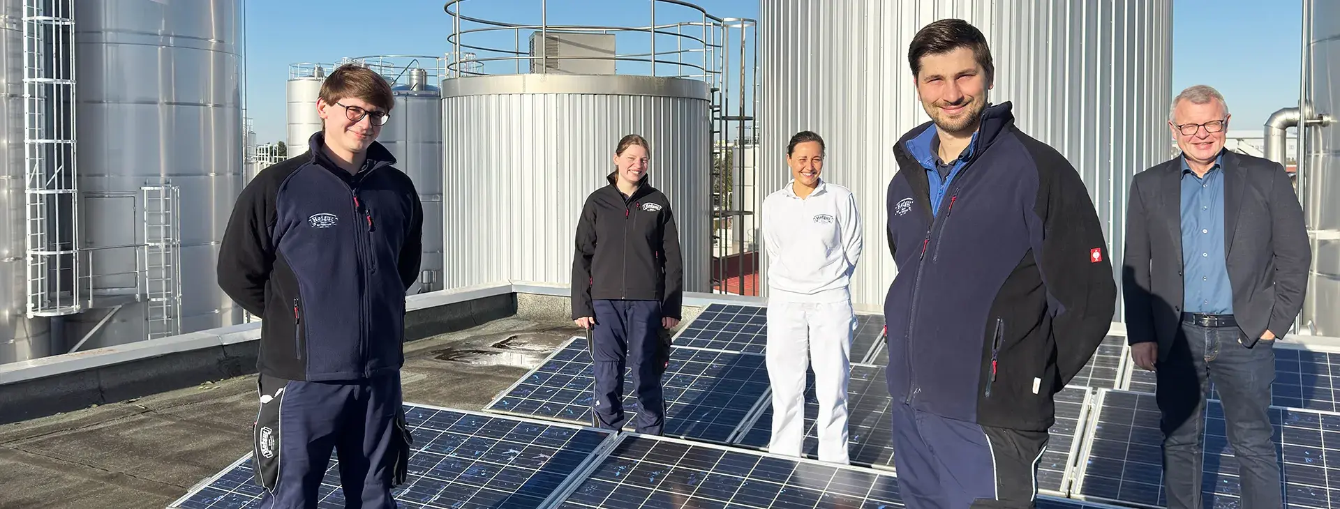 Das Nachhaltigkeitsteam der Hohenloher Molkerei auf dem Dach der Molkerei zwischen Solarpanelen