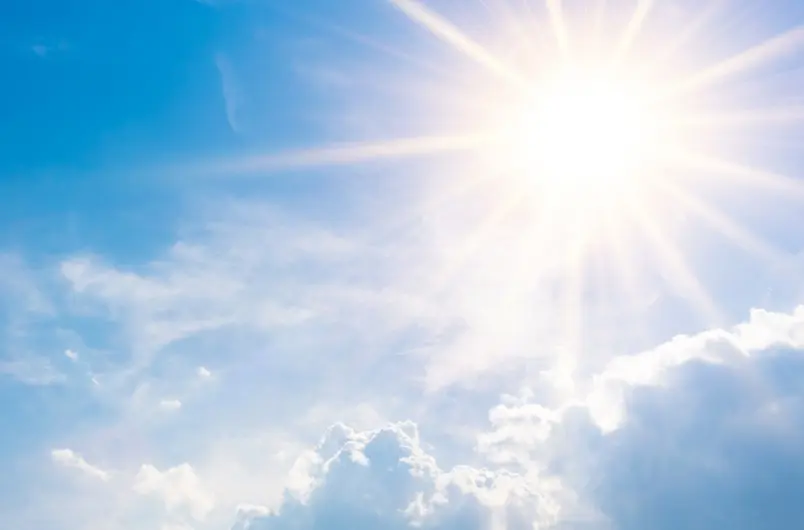 Helle Sonnenstrahlen am blauen Himmel mit einzelnen weißen Wolken am unteren Bildrand